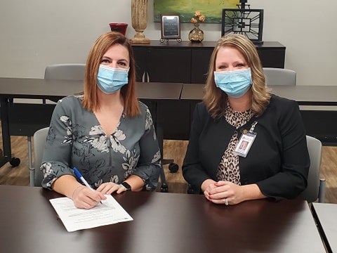 Two women sitting at desk wearing face masks