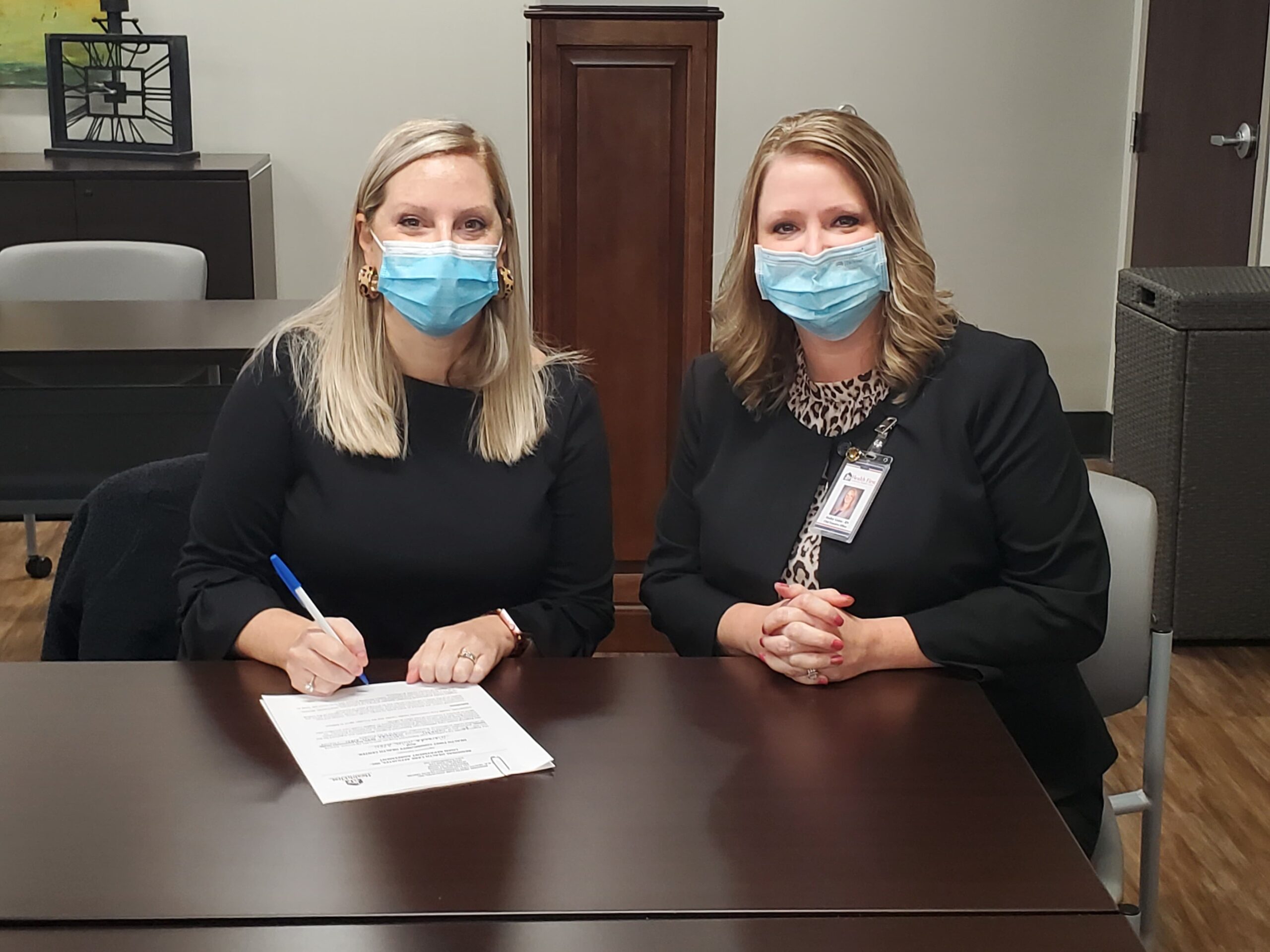 Two women wearing a face mask while sitting at a desk